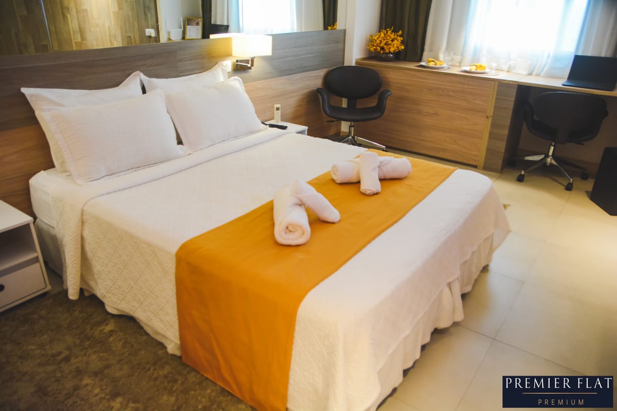 Cama de casal com lençóis brancos e toalhas dobradas no Premier Flat Premium